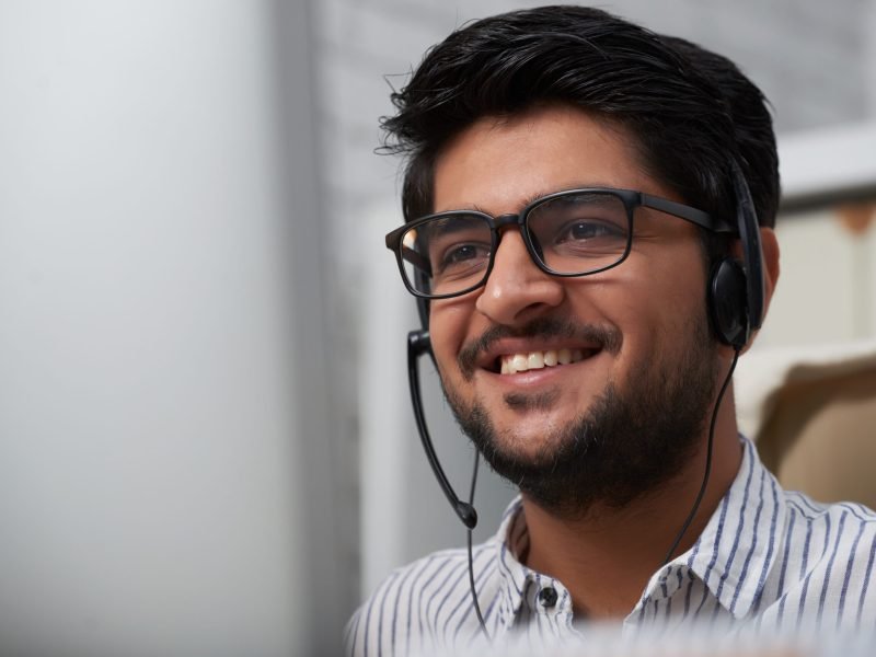 Face of cheerful Indian consulting service manager talking client via headset